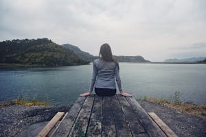 Frau sitzt auf Holzplanken und genießt den friedlichen Blick auf einen Bergsee, umgeben von Natur und Ruhe.