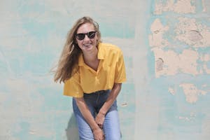 Lässige junge Frau, die in Sonnenbrille lächelt und vor einer vintage-bunten Wand posiert.