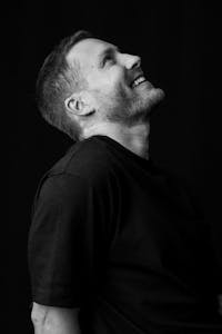 Monochromes Porträt eines Mannes, der lächelt und nach oben blickt.