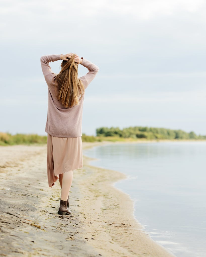 Eine Frau genießt einen friedlichen Spaziergang an einem Strand am Seeufer und verkörpert Entspannung und Freiheit.