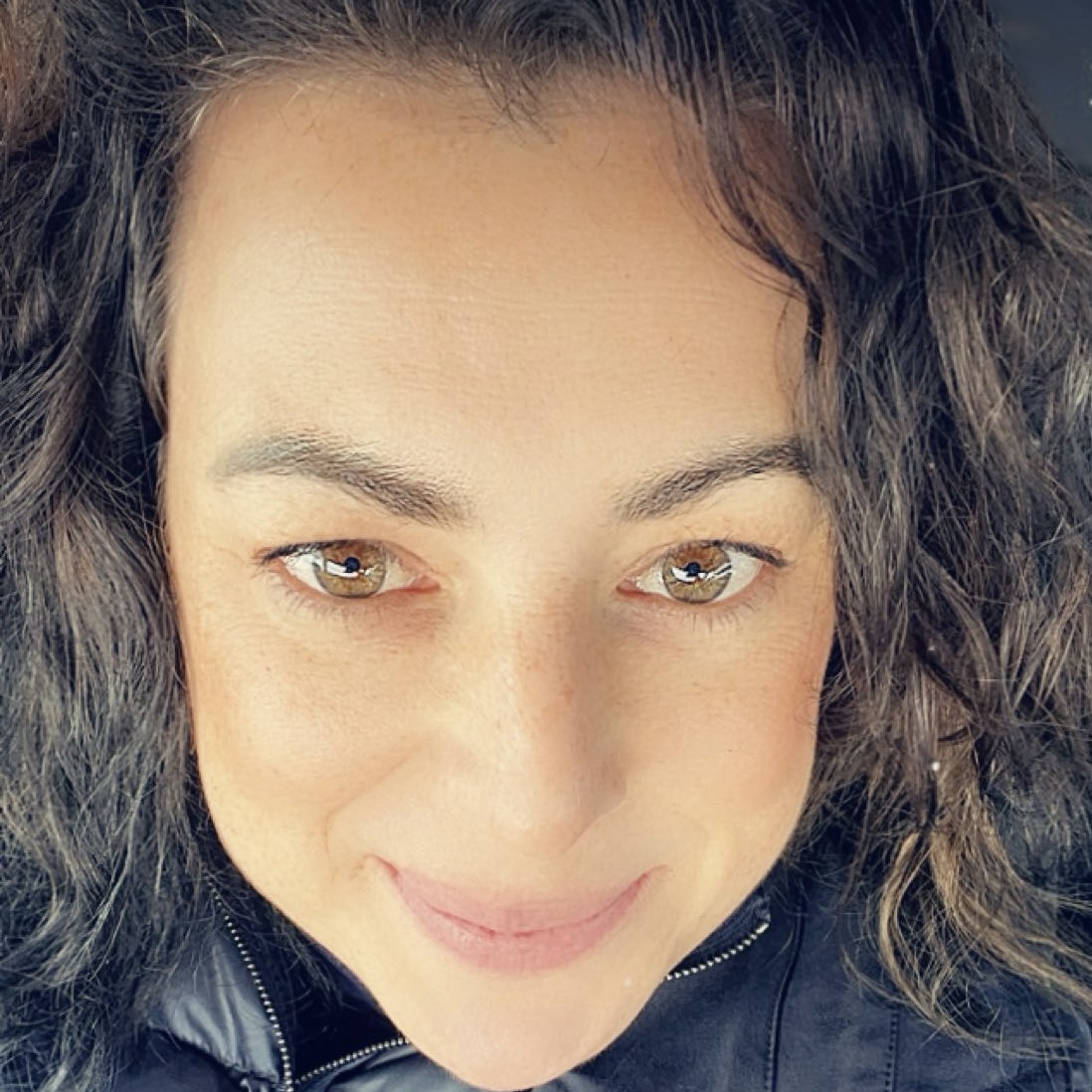 Porträt von Jule, lächelnd mit French-Bob, Locken und blauer Jacke.