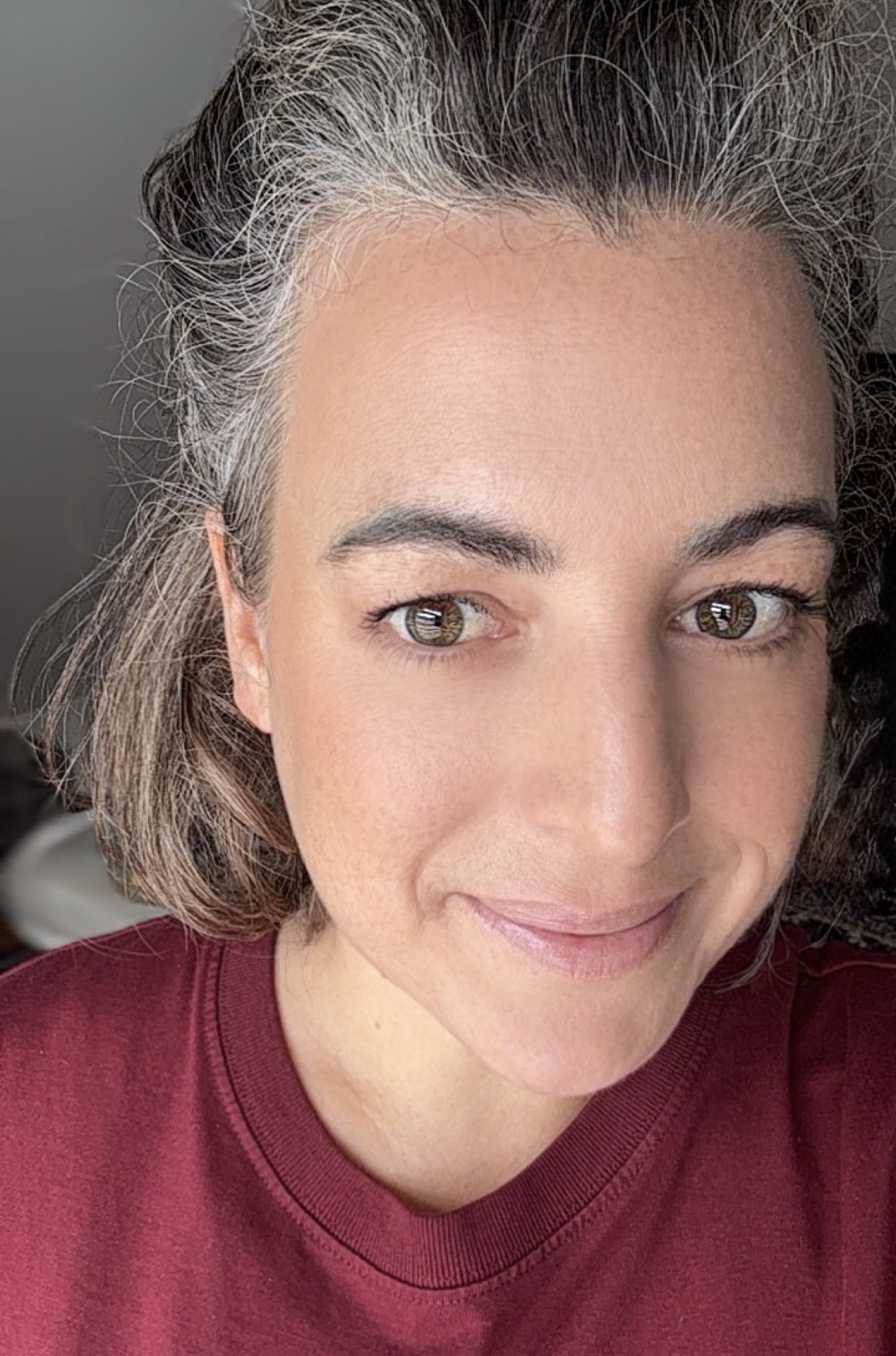 Porträt von Jule, lächelnd mit French-Bob. Bordeauxfarbenes Shirt im Hintergrund Therapie-Zimmer